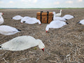 A group of white snow goose silhouette decoys with a heavy duty silhouette decoy storage bag in a stubble field.